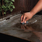 The liquid restorer being applied to a cool steel cooking surface to break down outdoor grill grime.