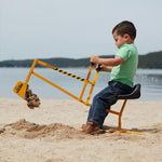 Child playing with The Big Dig ride-on excavator in a sandbox