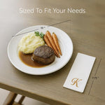 Close up of cursive gold letter K on white linen-feel napkin