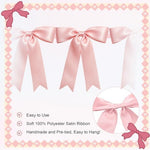 Two pieces of pastel pink bow decorations hanging elegantly across a white wall