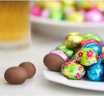 Assorted vibrant solid and floral printed Italian foiled mini milk chocolate eggs arranged together.