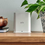 Arlo wireless base station with integrated smart siren placed next to home router network equipment setup.