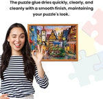 Wide plastic spreader tool applying clear glossy liquid evenly across a colorful one thousand piece tabletop jigsaw.