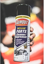 Gumout imported USA automotive maintenance spray can placed next to a vehicle carburetor and brake rotor setup.