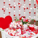 Romantic photo booth setup featuring layered rose gold and red heart streamers