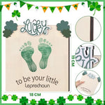 Beeveer newborn footprint keepsake disc styled as a photography prop next to baby clothes.