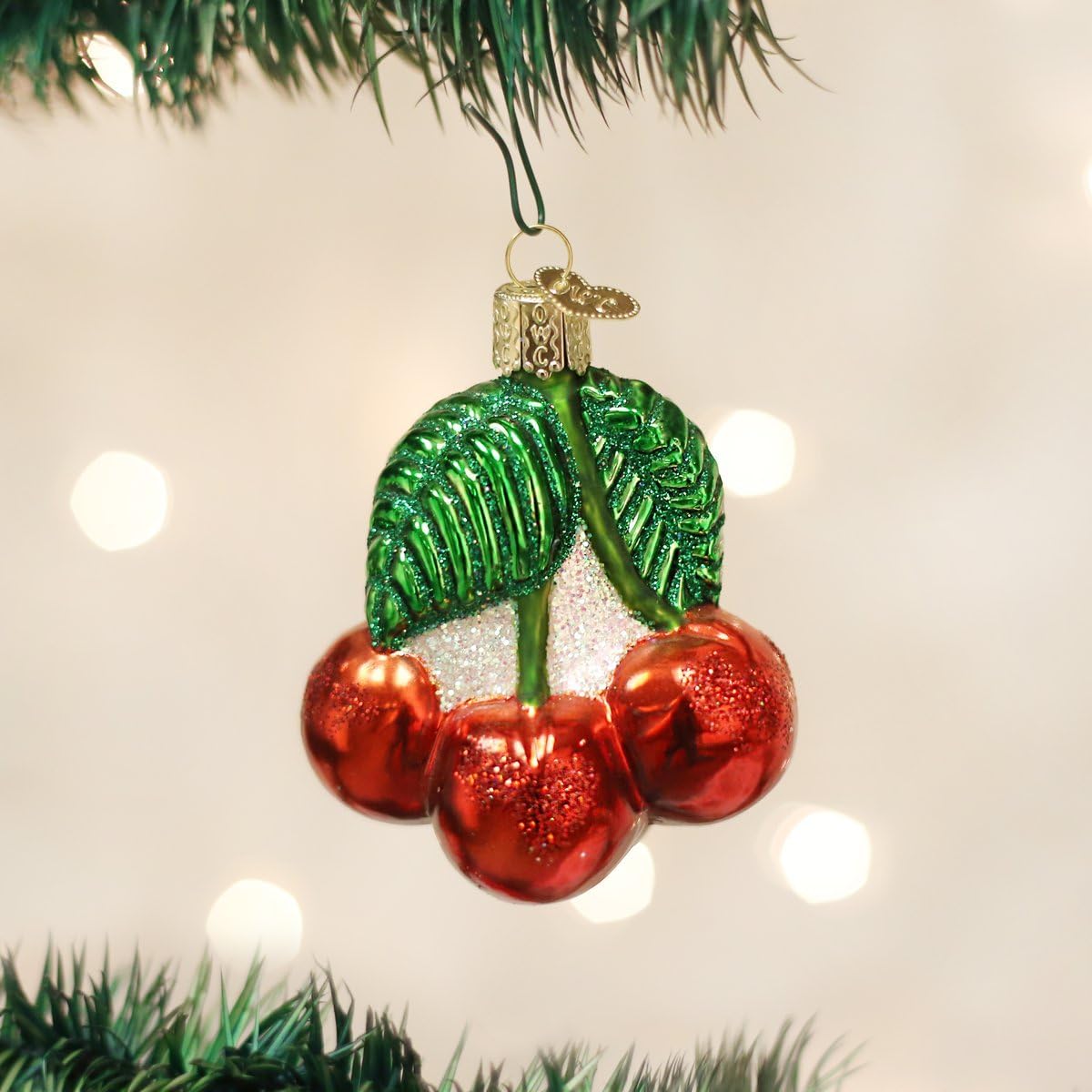 Close up of hand painted glossy red cherries glass ornament with green glitter leaves