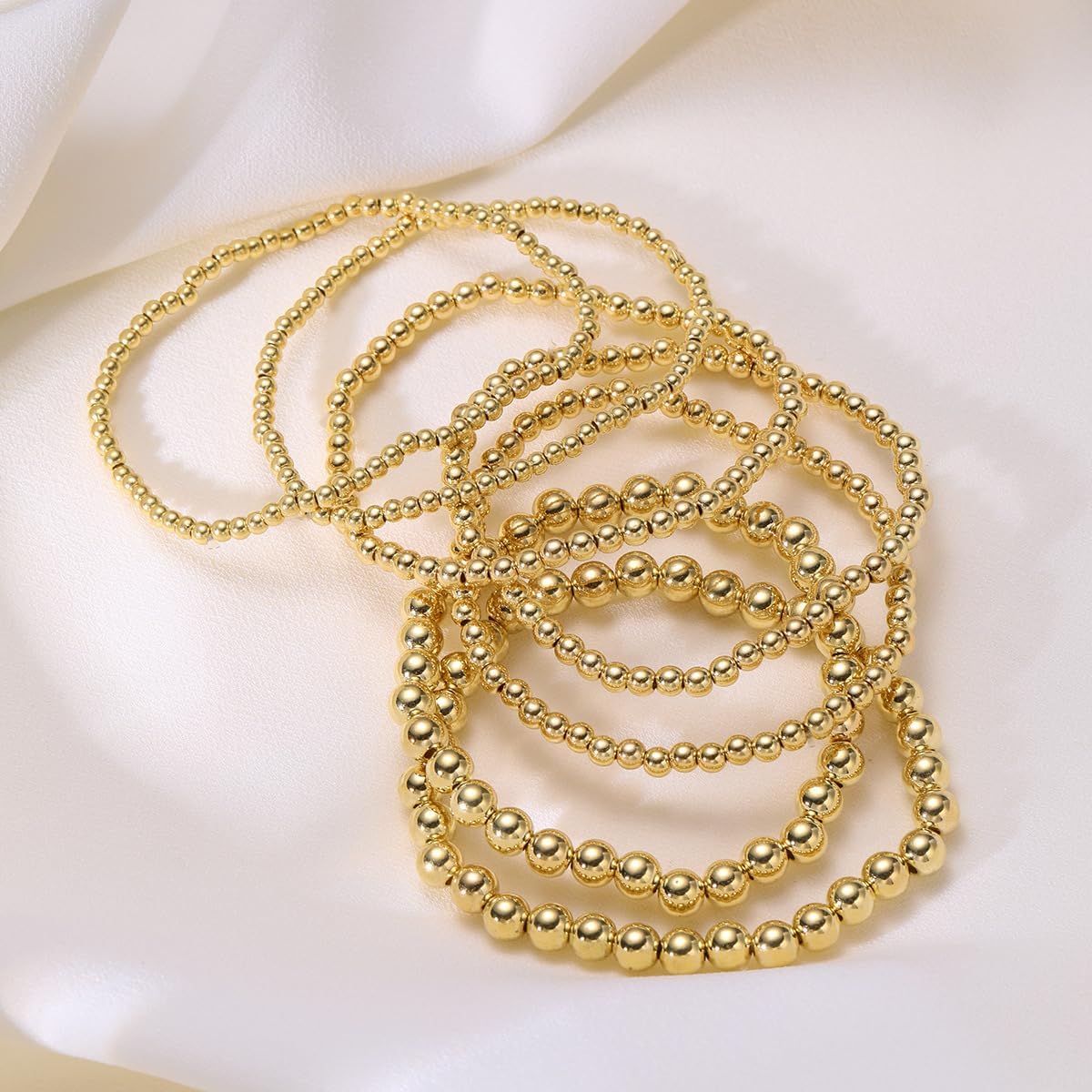 Stackable gold beaded bracelets displayed flat on a neutral surface.