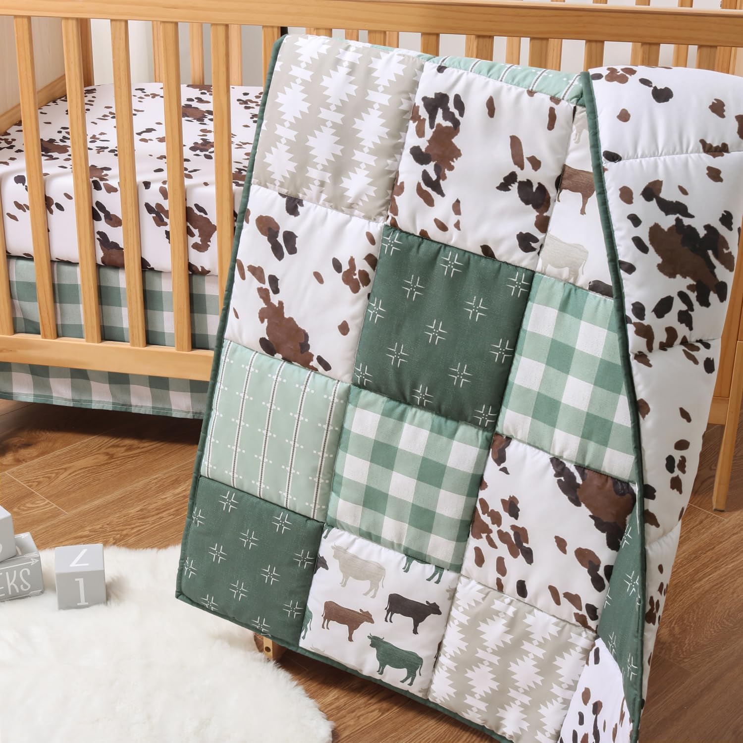The Peanutshell Boho Farm baby crib bedding set showcasing front view of green patchwork quilt and cow print sheet.