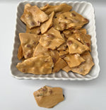 Irregular golden pieces of SweetNest buttery caramel peanut brittle displaying a light bubbly texture loaded with roasted peanuts