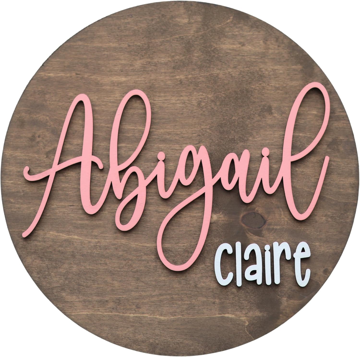 HickoryHollowDesigns custom round nursery name sign featuring pink script typography on a circular wooden backdrop for a baby girl room.