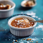 Single unwrapped caramel square next to sea salt crystals showcasing the sweet and savory ingredients.