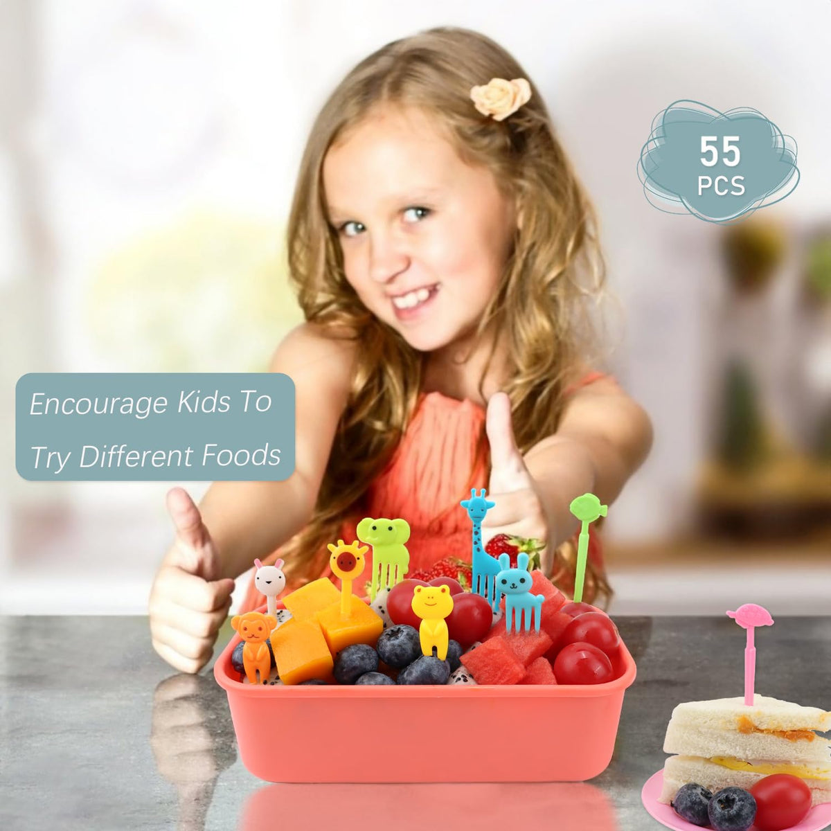 Pack of toddler food forks arranged beside a healthy school tiffin box containing diced fruits and sandwiches.