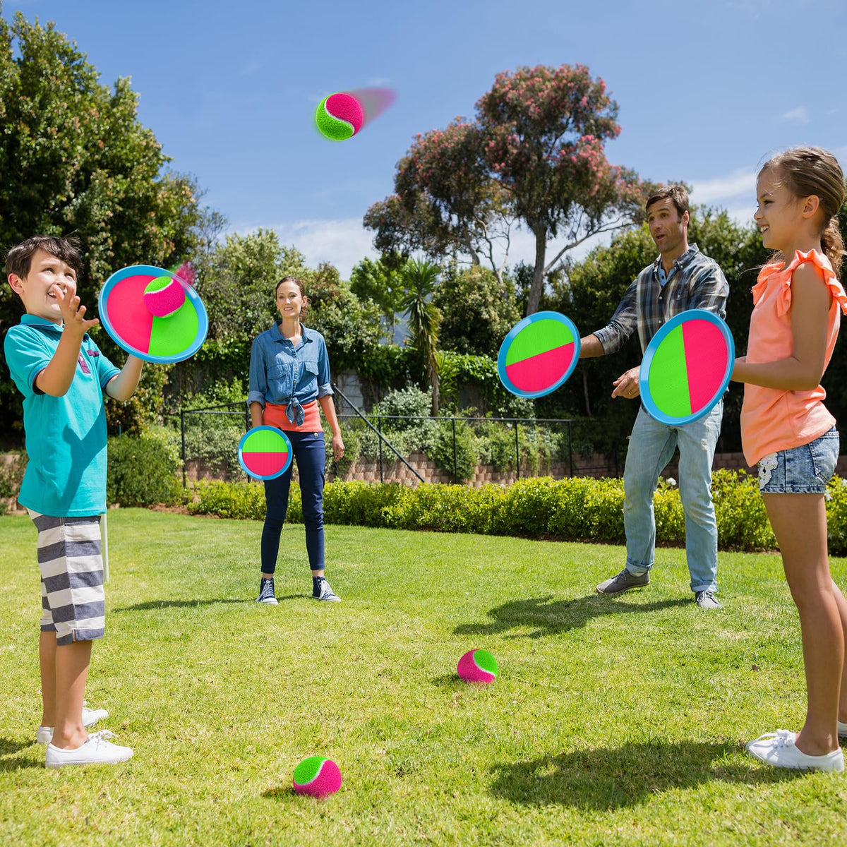 Four vibrant blue and pink sticky catch paddles laid out with matching play balls for outdoor yard games.