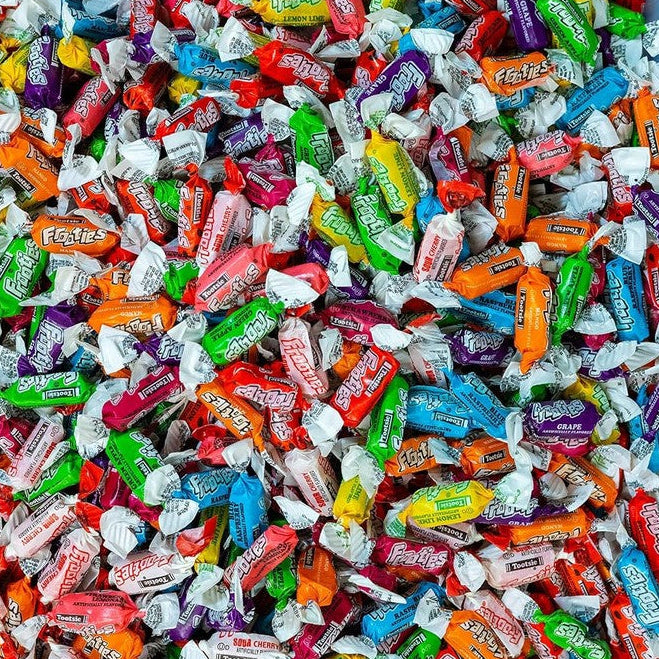 A close-up, top-down view of a large pile of individually wrapped Reese's candies in various colors and flavors, filling the frame.