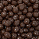 A close-up pile of glossy dark brown chocolate-covered round candies or chocolate pearls filling the frame.