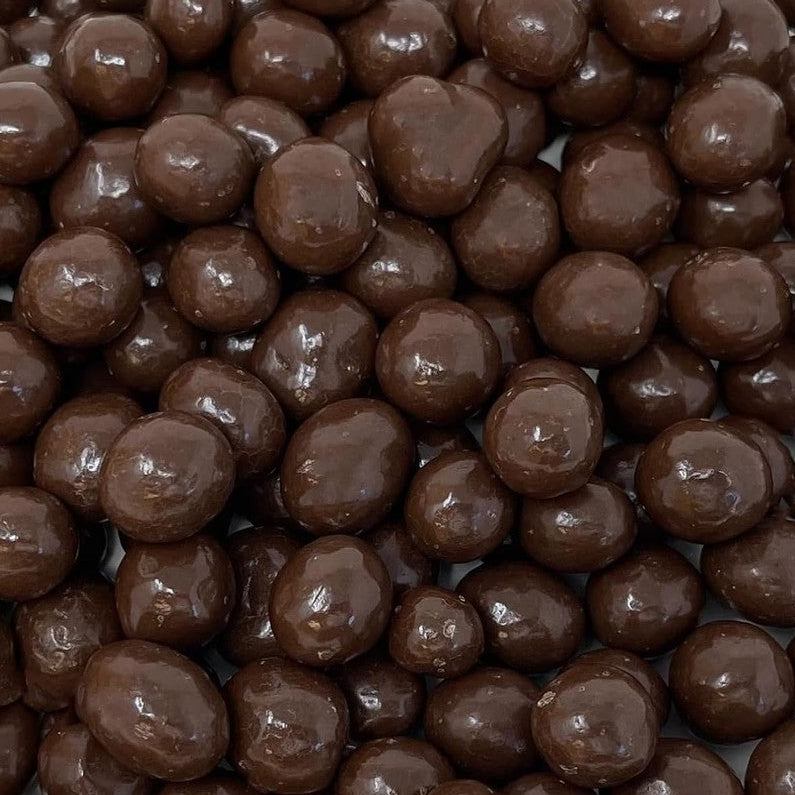 A close-up pile of glossy dark brown chocolate-covered round candies or chocolate pearls filling the frame.