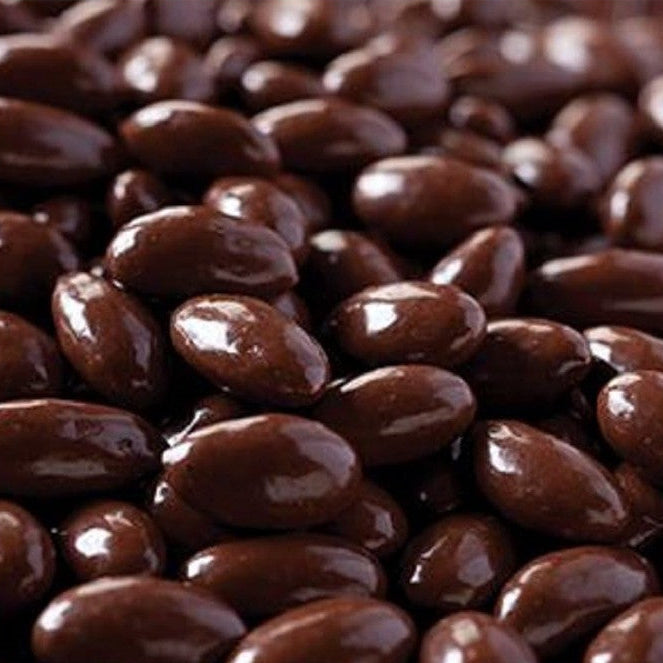 A close-up pile of glossy dark brown chocolate-covered almonds or candy-coated nuts filling the frame.