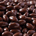 A close-up pile of glossy dark brown chocolate-covered almonds or candy-coated nuts filling the frame.